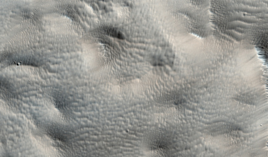 塔尔西斯山群（Tharsis Montes）附近看上去很模糊的地貌。乍看上去，你或许以为此图的某些部分焦点没对准。但是，正如我们看到的像陨石坑那样更加清晰的地形，图像模糊不是人为因素造成的，而是极为平滑表面的特征。平滑表面是因一层像毯子一样铺在地貌上的厚厚尘埃所致。