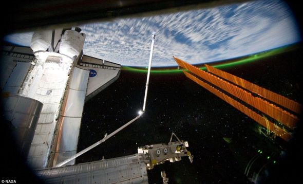 照片由国际空间站上的“亚特兰蒂斯”号宇航员14日晚上拍摄，呈现了航天飞机后面的绚丽的绿色南极光