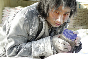 这位工人抱着一个水杯在成品大白粉堆上发呆。（图片来源：天山网） 