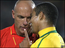 A referee pointing at a football player's mouth
