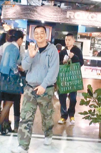 王喜面对镜头挥手微笑，好友明仔则负责拿袋子