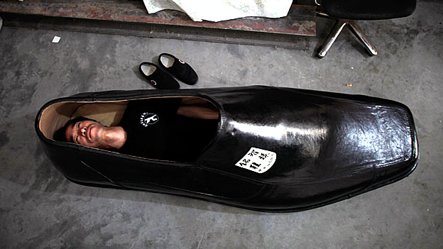 A man lies inside a giant shoe.